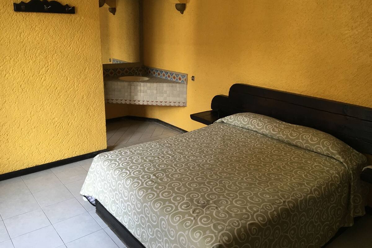 A room with a bed, a bathroom with a sink, and a yellow wall.