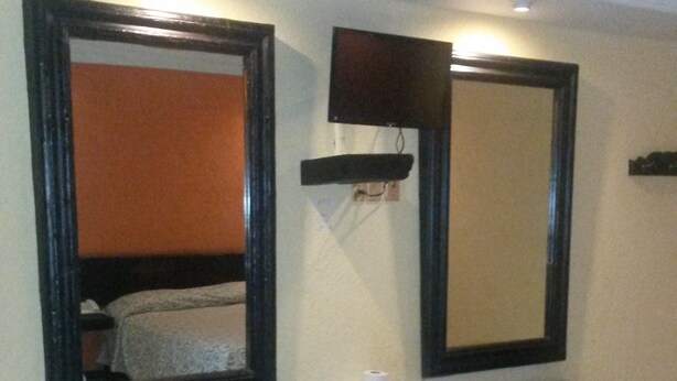 Habitación de hotel con una cama grande, un banco de madera oscura y dos espejos grandes en la pared.