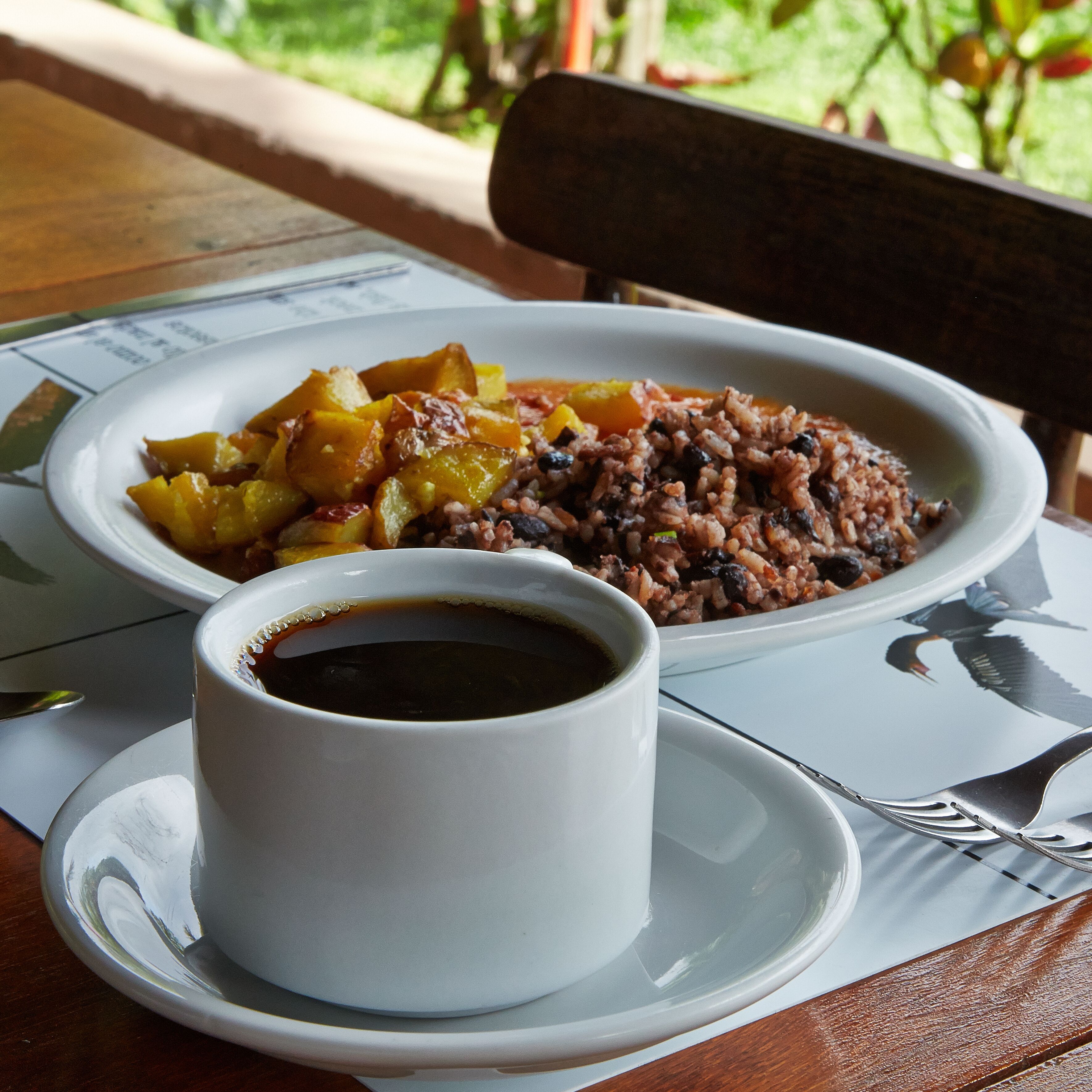 A meal consisting of rice, beans, and vegetables on a plate, accompanied by a cup of coffee on a saucer.