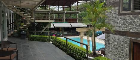 A covered outdoor area with a pool, stone flooring, and outdoor seating.