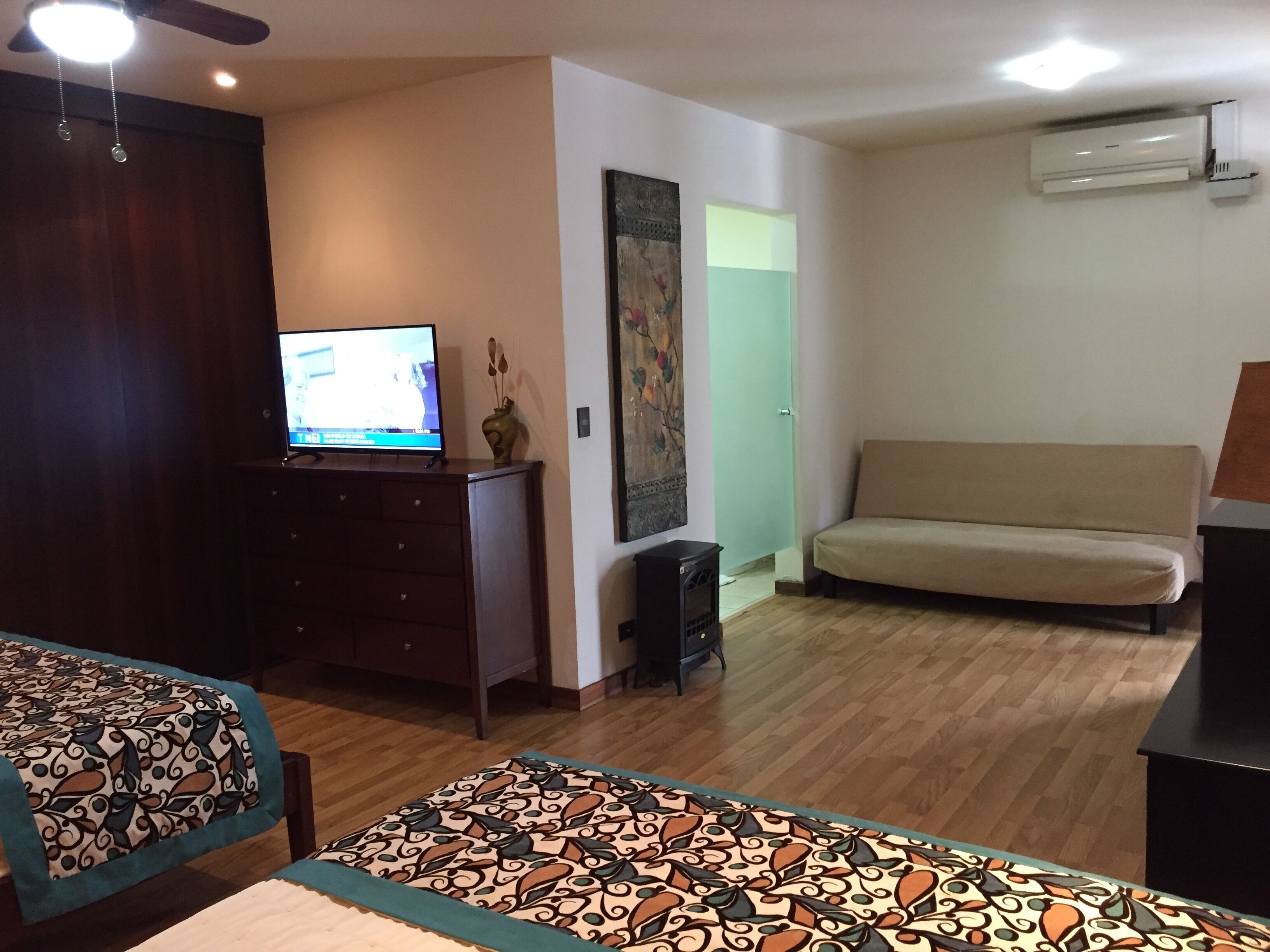 A room with a television on a wooden cabinet, a sofa, a patterned rug, and a ceiling fan.