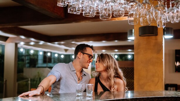 Een koppel in een bar met een modern interieur, waaronder een hoog plafond en hangende lampen.