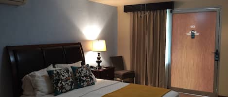 A hotel room with a bed, a bedside lamp, a ceiling fan, a door, and a nightstand.