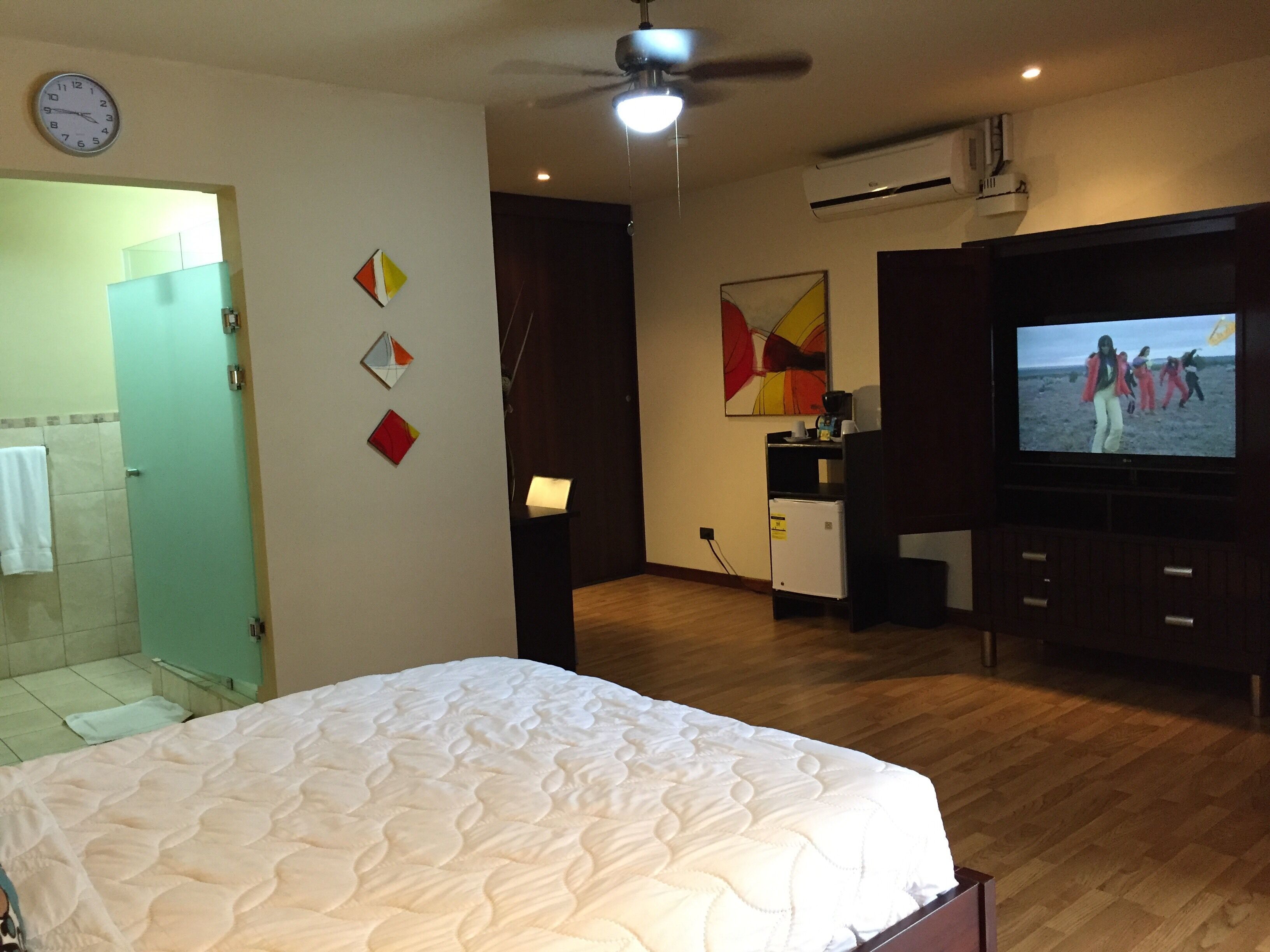 Ein Hotelzimmer mit einem Bett, einem Fernseher, einem Deckenventilator und einer Wanduhr.