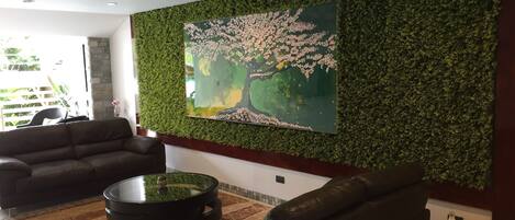 Una sala de estar moderna con pared verde, un cuadro grande y una mesa de centro redonda.