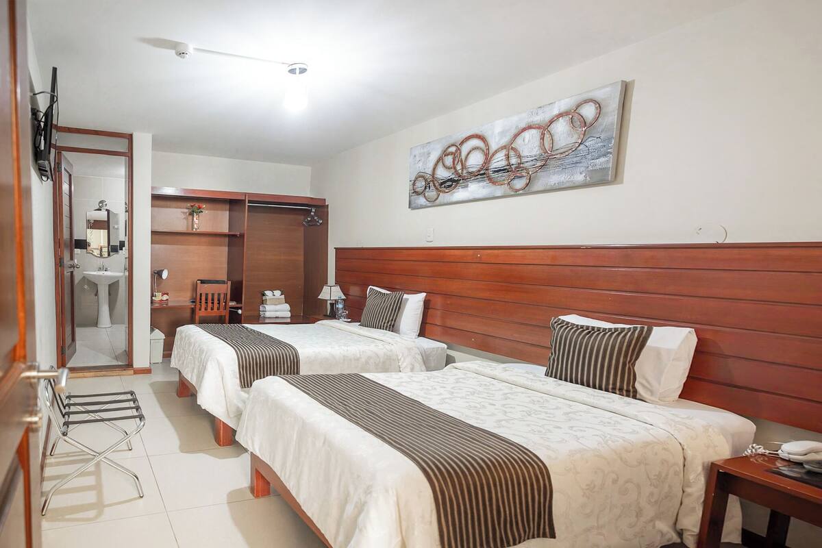 A hotel room with two beds, a wooden headboard, a painting on the wall, and a bathroom visible through an open door.