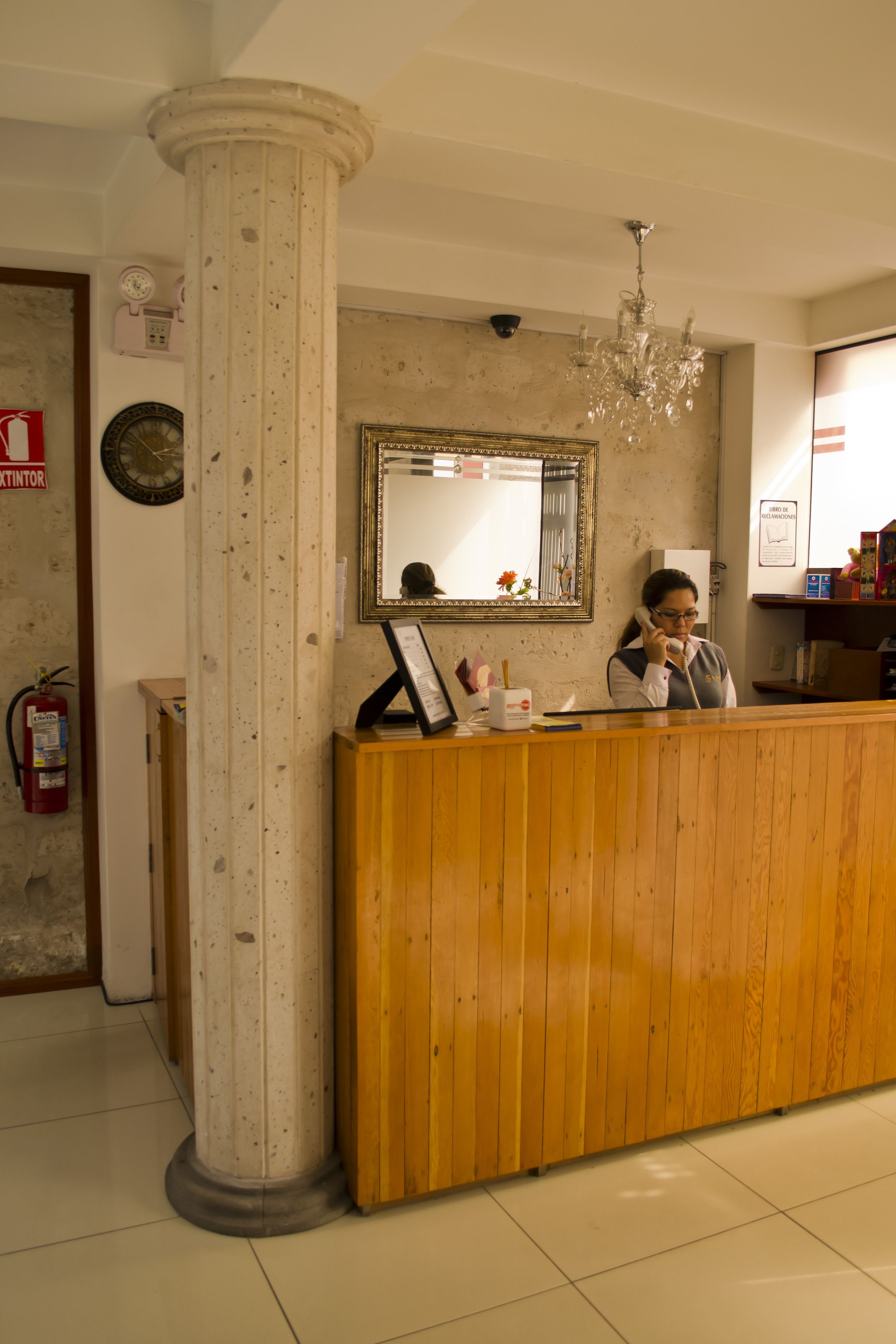 A reception desk with a wooden finish, a large mirror above it, and a chandelier hanging from the ceiling.