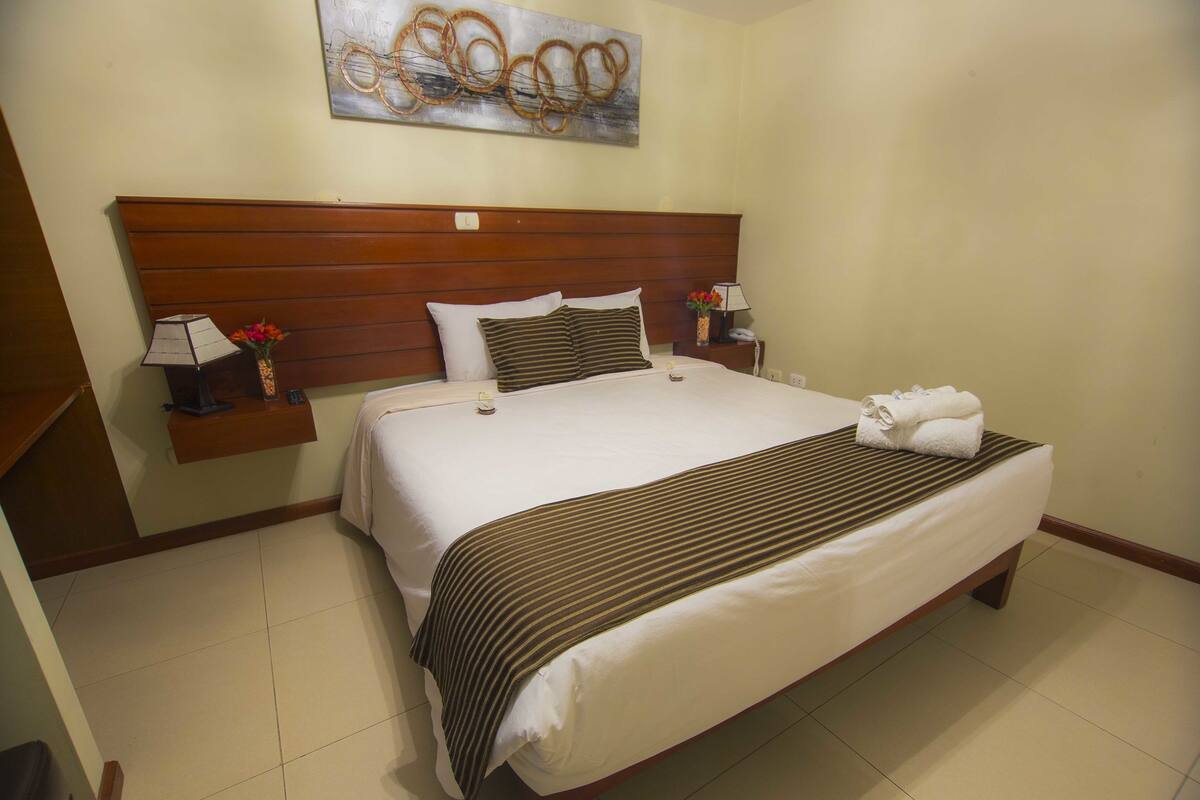 A neatly made bed with a striped bedspread, a wooden headboard, and a wall-mounted artwork above.