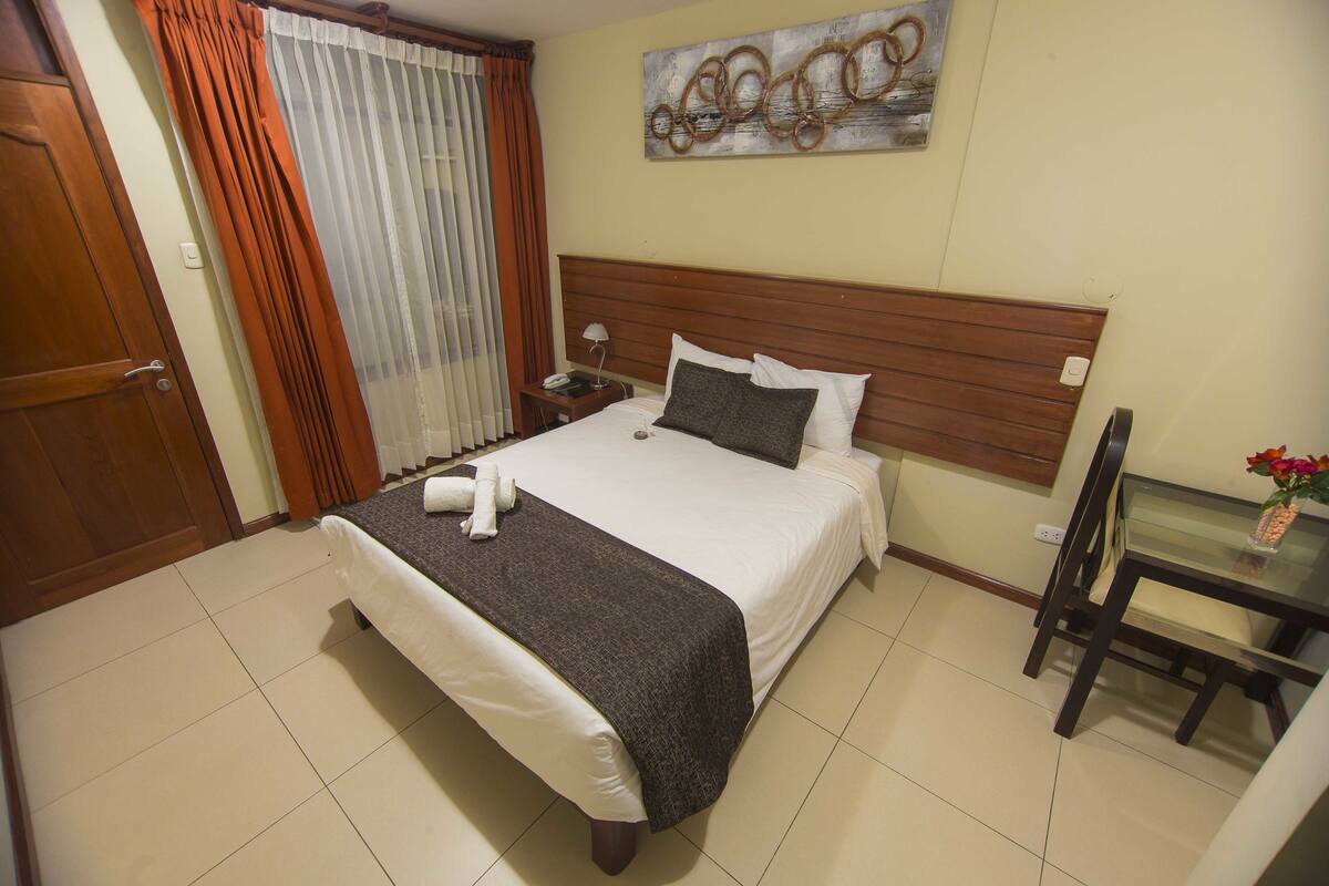 A neatly made bed with a wooden headboard, a bedside table with a lamp, and a small table with a vase of flowers.