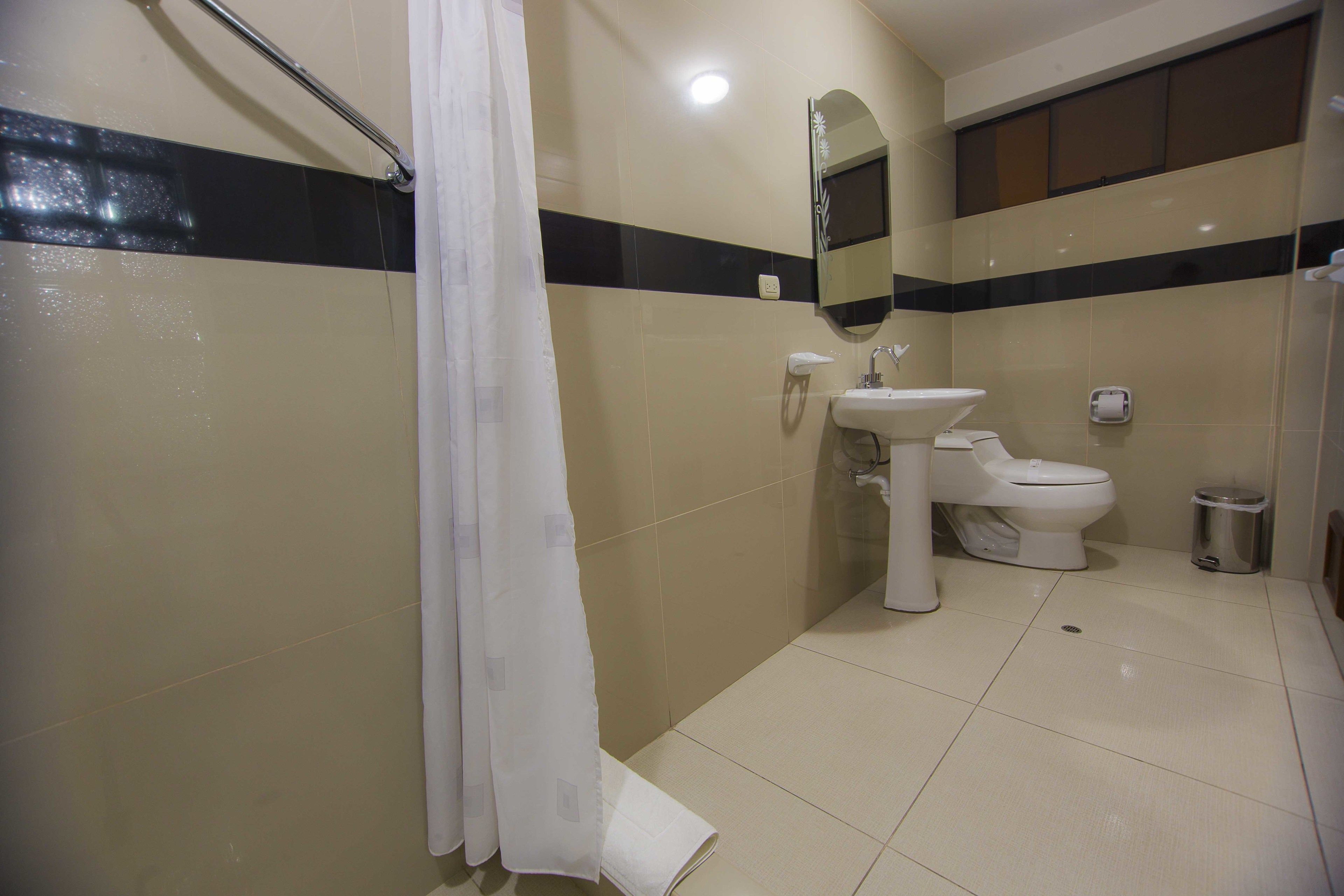 A bathroom with a shower, sink, toilet, and a trash bin.