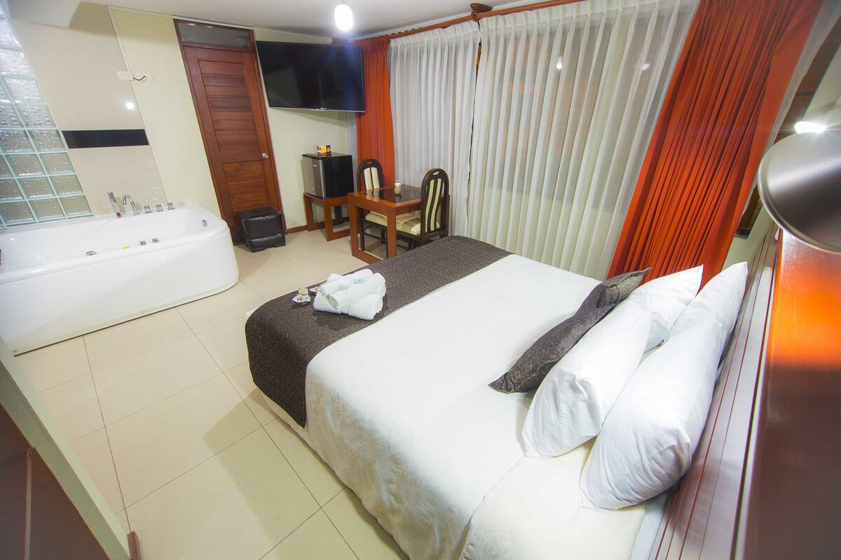 A hotel room with a large bed, a separate bathroom with a bathtub, a desk with a chair, and a TV mounted on the wall.