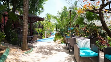 Un resort tropical con piscina, mobiliario de mimbre y exuberante vegetación.