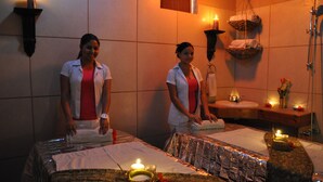 A spa room with two massage tables, towels, candles, and a small sink. - West Bay Lodge (Roatan)