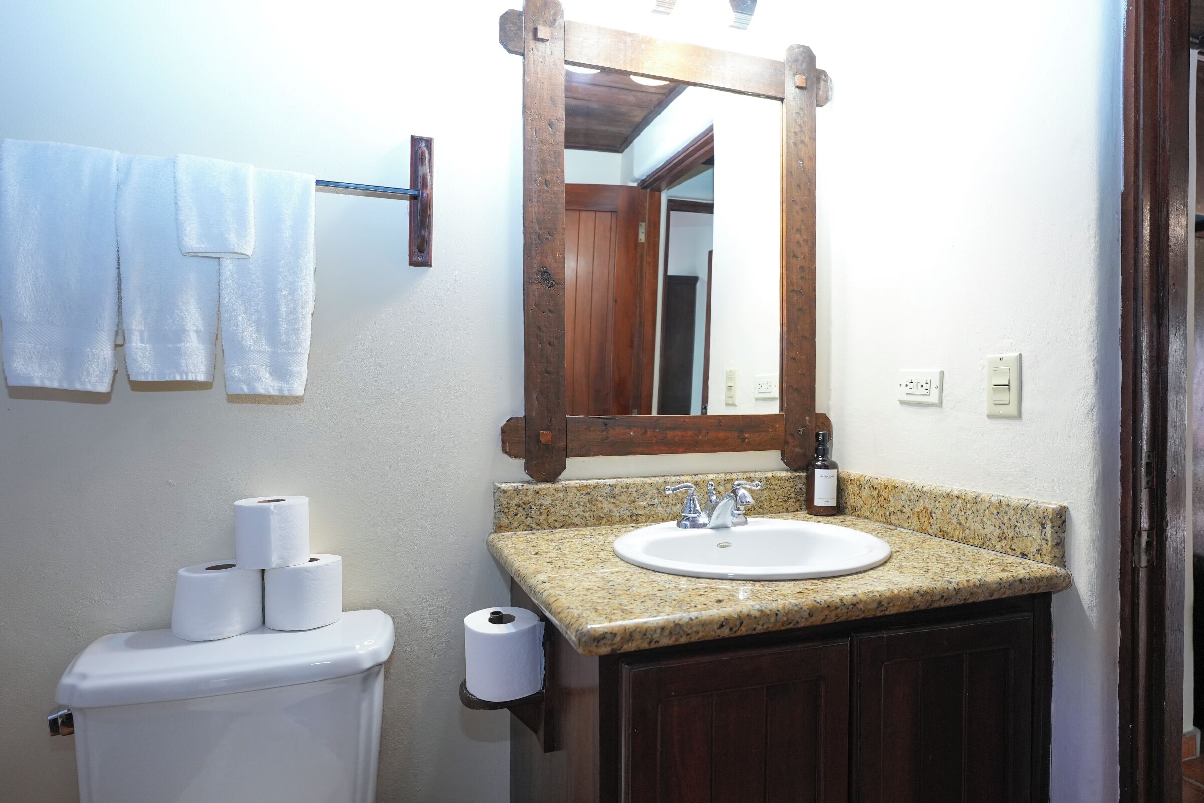 Un baño con inodoro blanco, lavamanos con encimera de granito y espejo con marco de madera.