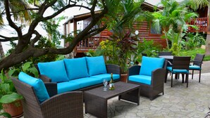 A patio area with wicker furniture, including a sofa and chairs, and a table with a bottle and glass. - West Bay Lodge (Roatan)