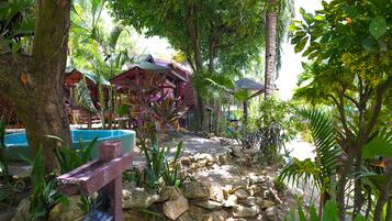 Un jardín tropical con un sendero de piedra, estructuras de madera y abundante vegetación.