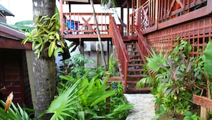 A wooden staircase leading to a balcony with a metal railing, surrounded by lush tropical plants. - West Bay Lodge (Roatan)