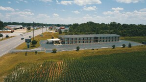 A motel with a large parking lot, a road in the foreground, and a cornfield in the background. - Economy Inn (Rogersville)