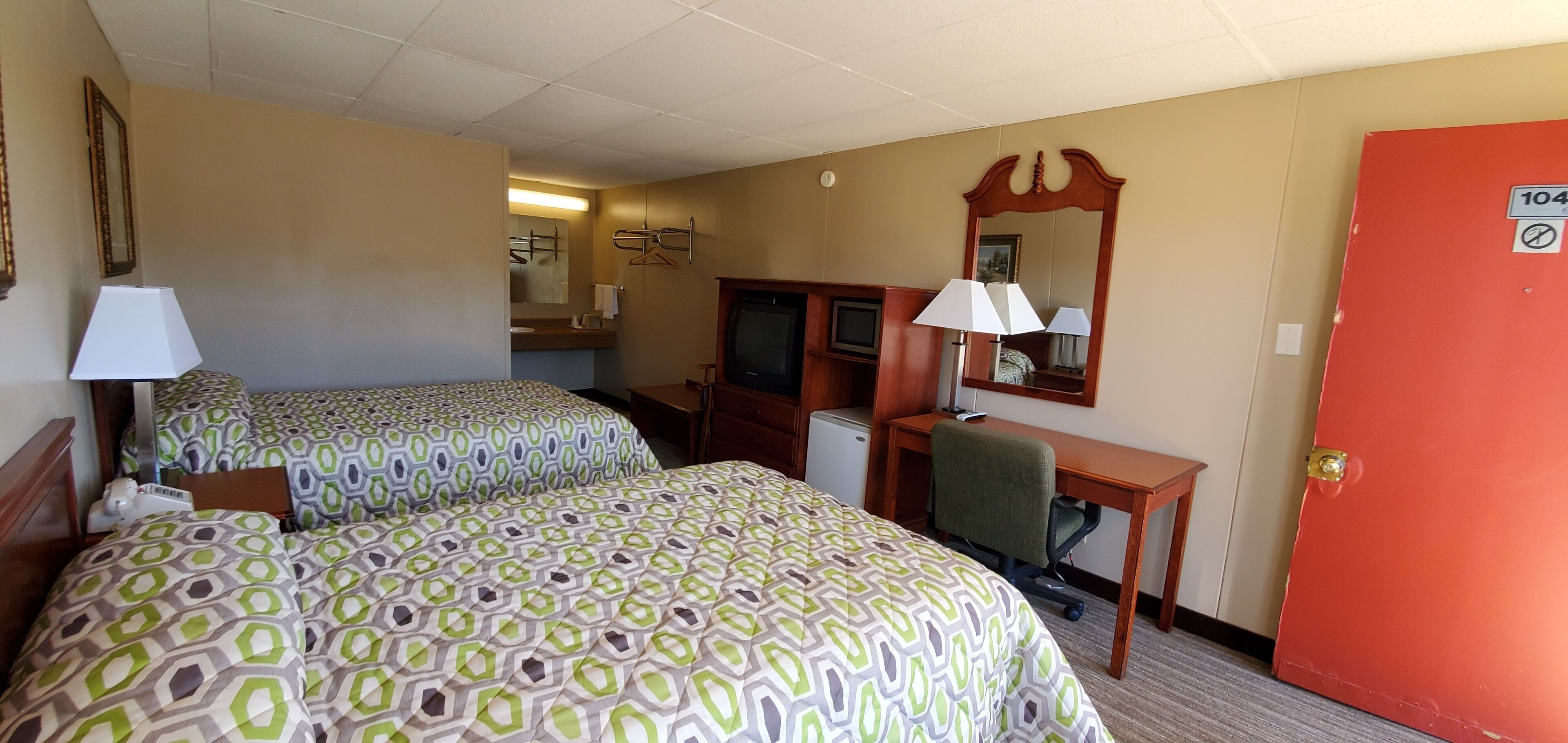 A hotel room with two beds, a desk, a chair, a television, and a mirror.