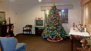 A living room with a Christmas tree, a television, a chair, and a fireplace. - Lake Eufaula Inn (Checotah)