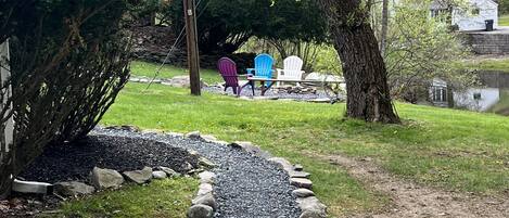 A gravel path bordered by rocks, leading to outdoor seating under trees.