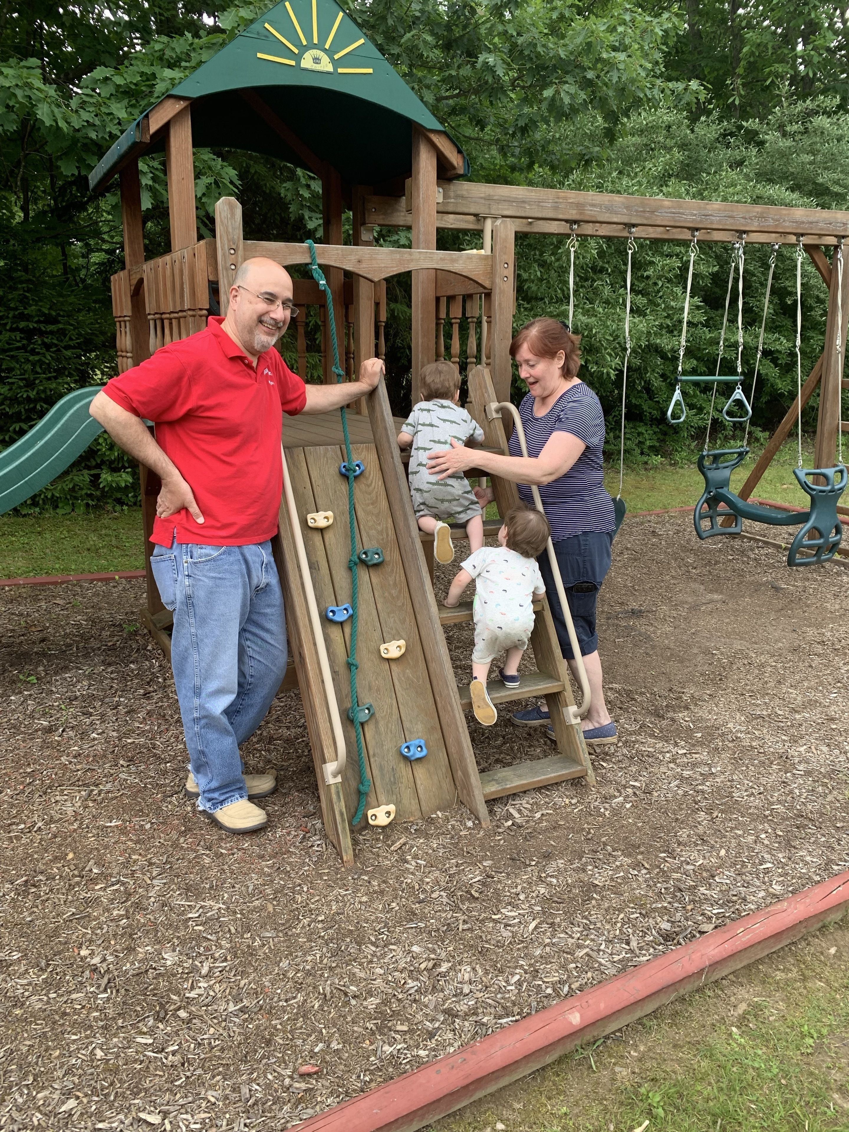 Une structure de jeu en bois, dotée d’un toboggan et d’un mur d’escalade, entourée de paillis et de verdure.