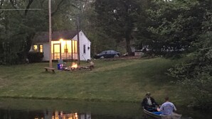 A house with a lit fire on the lawn, a dock, and a person in a boat. - Echo Valley Cottages (East Stroudsburg)