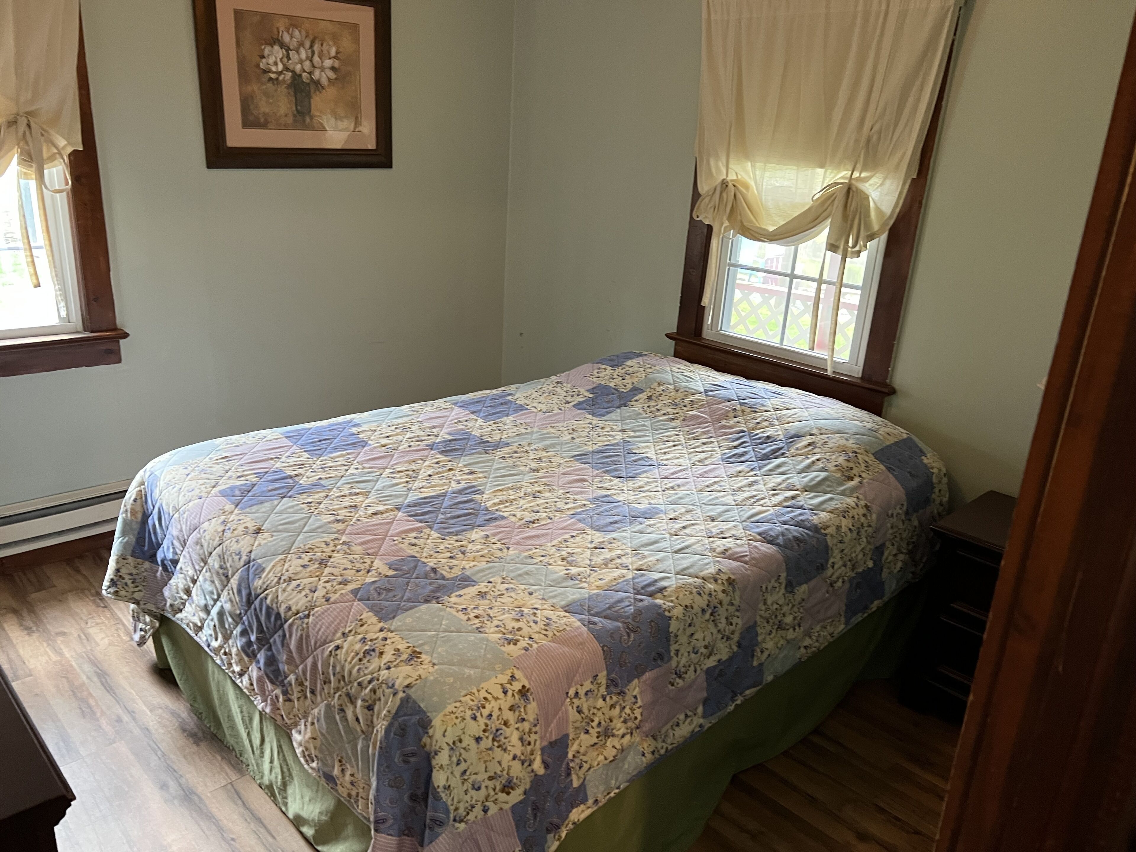 Une chambre à coucher avec un lit, une fenêtre avec des rideaux et un tableau encadré accroché au mur.