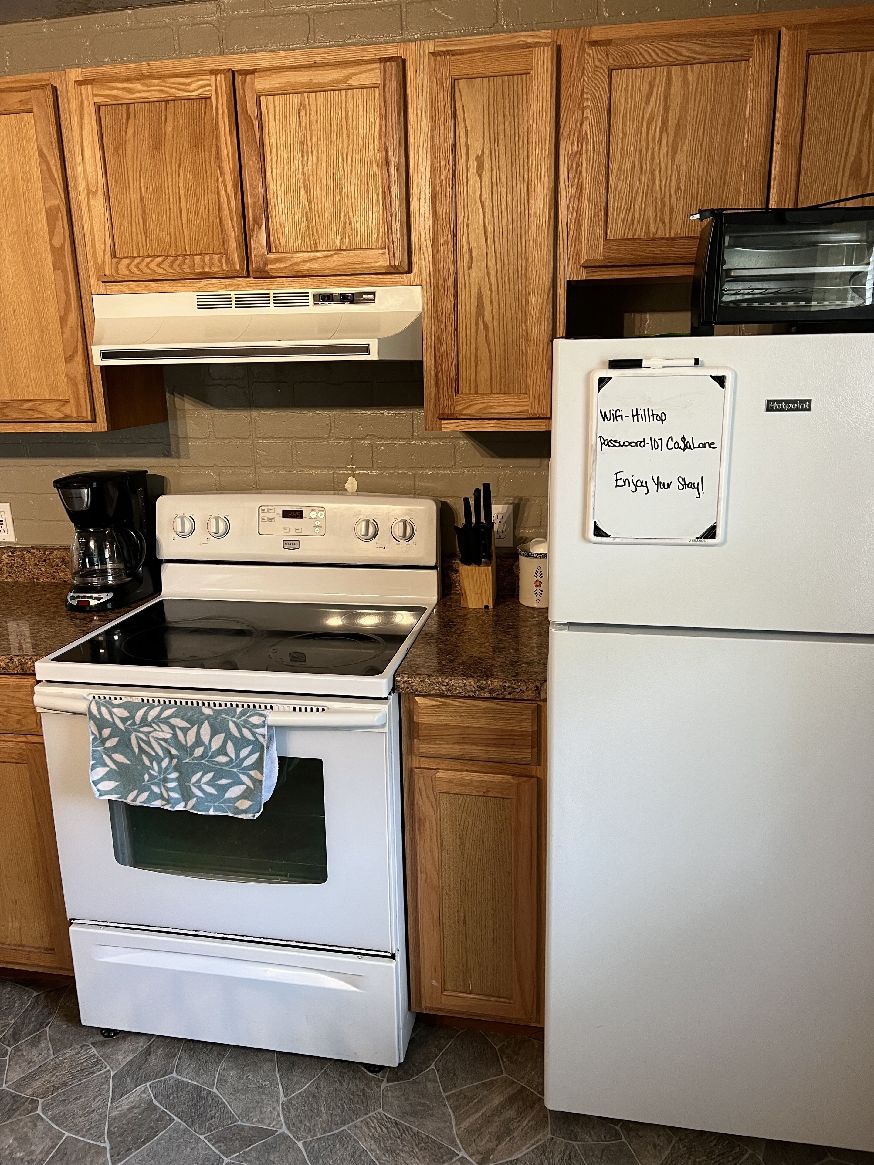 A kitchen with wooden cabinets, a white stove, and a refrigerator. There is a note on the refrigerator with Wi-Fi and password information.