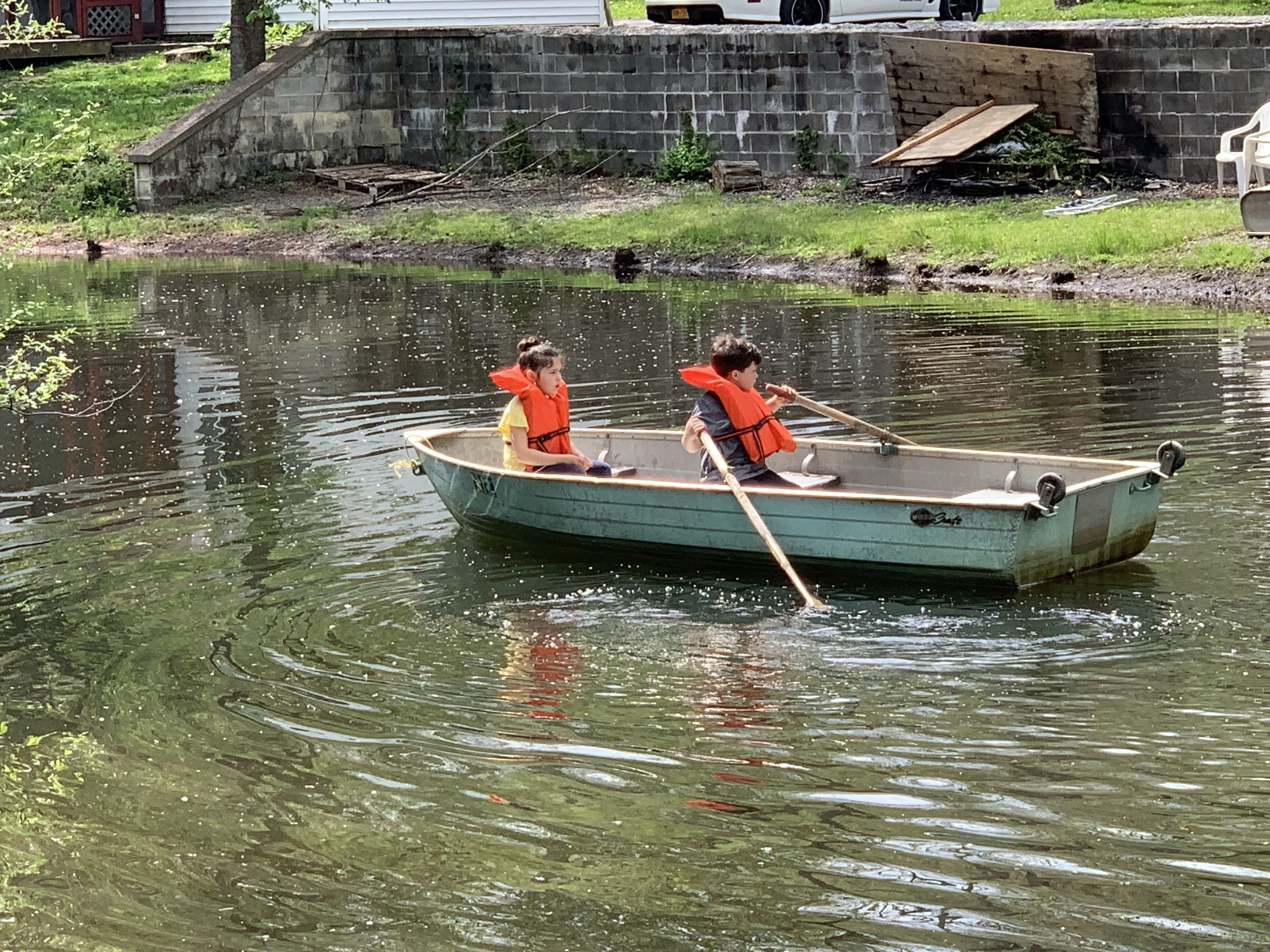 A small rowboat with two people paddling on a calm body of water.