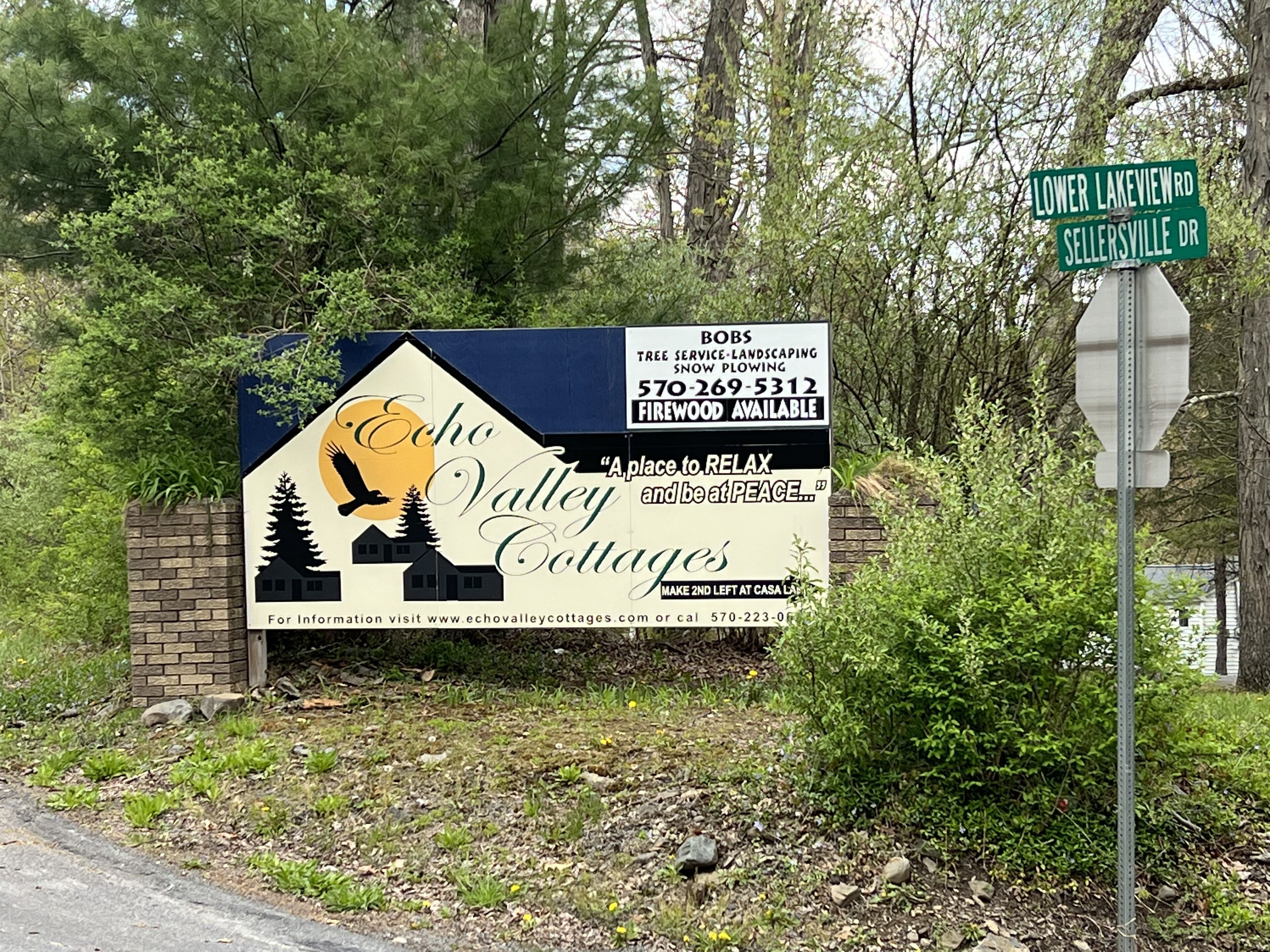 A roadside sign for Echo Valley Cottages advertising services like tree service, landscaping, and snow plowing.