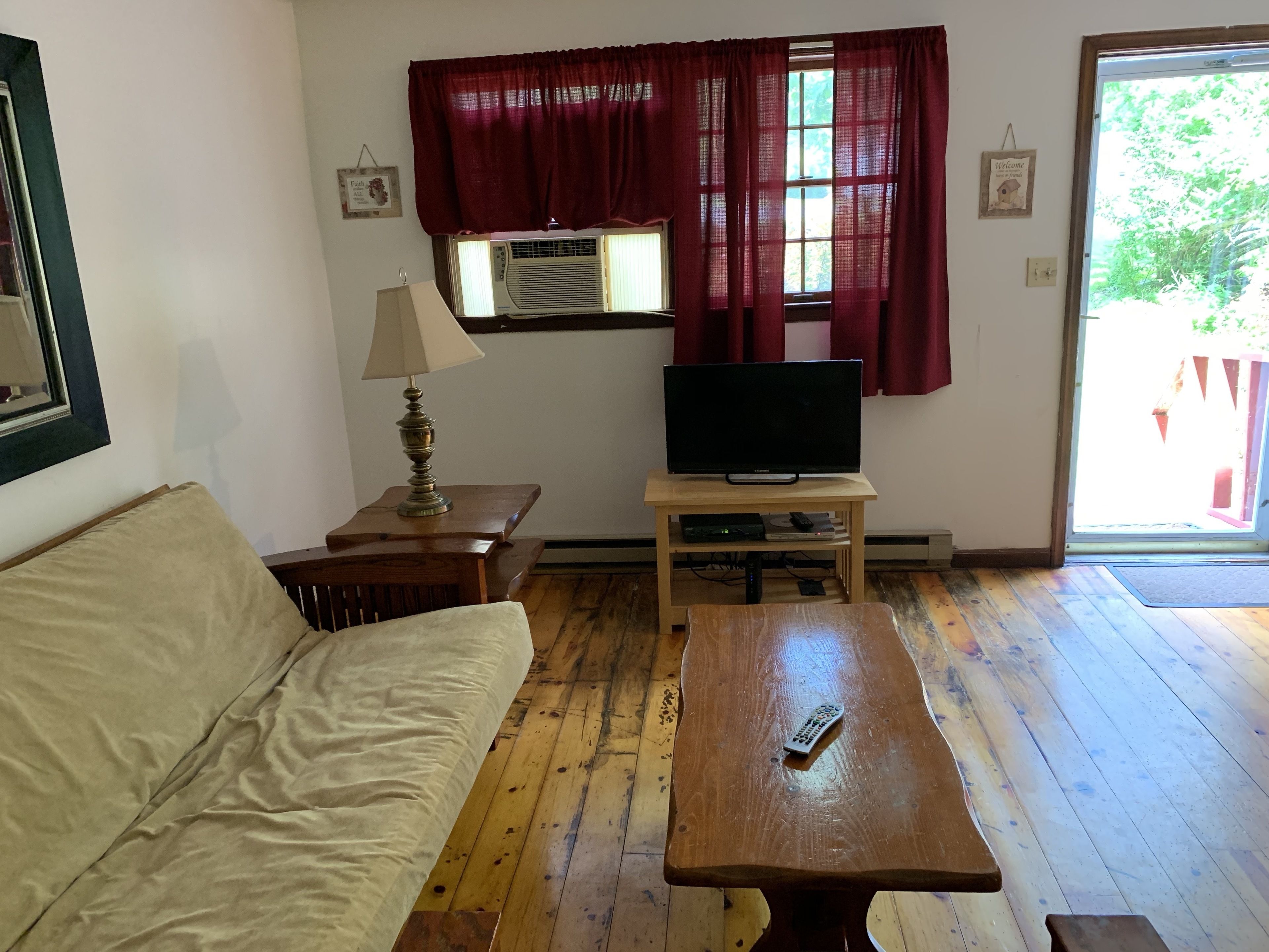 A living room with a sofa, a wooden coffee table, a TV on a stand, a lamp, and a window with curtains.