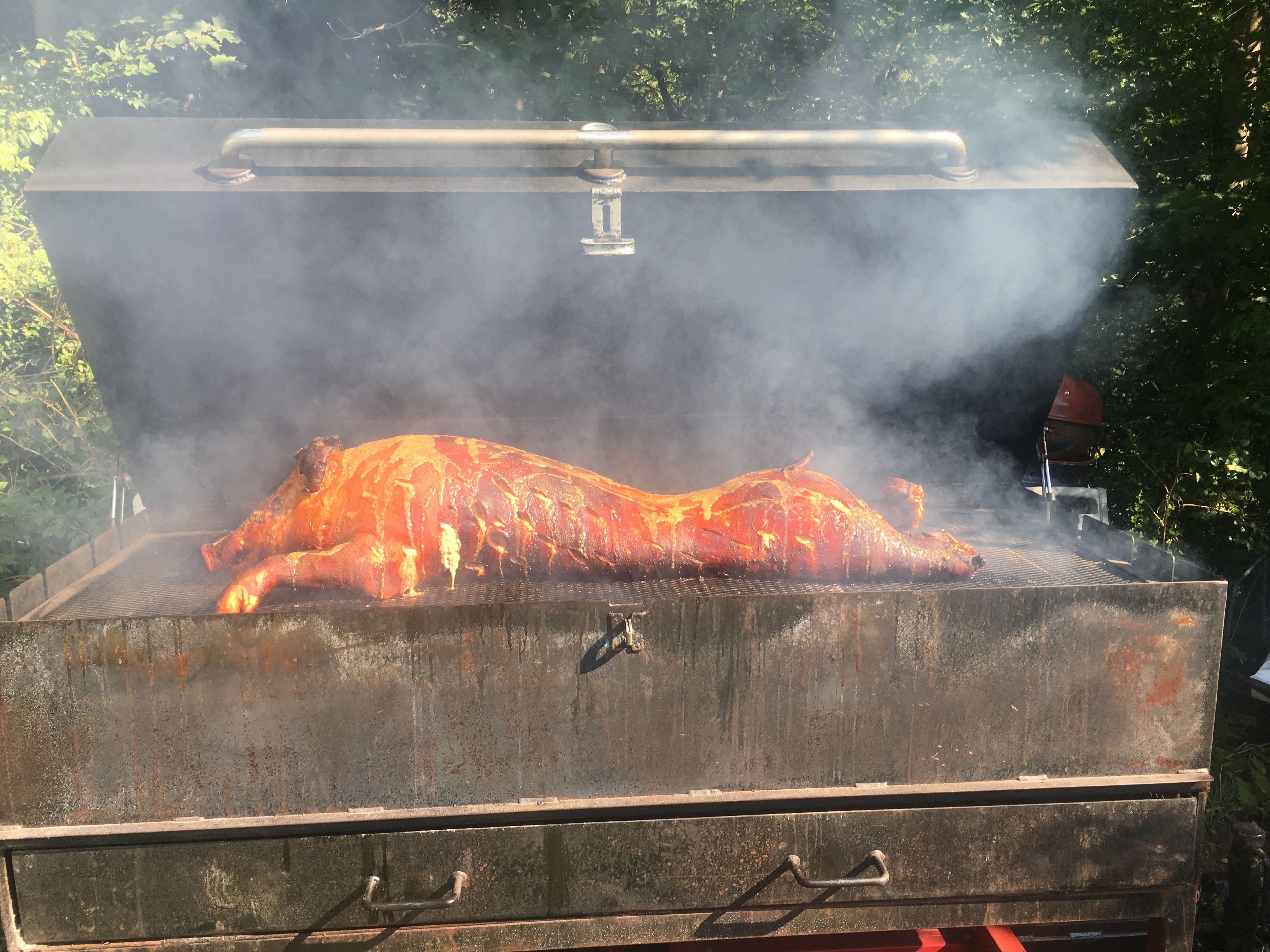 Een grote, industriële buitenbarbecue met een opvallend, dampend heel varken erop.
