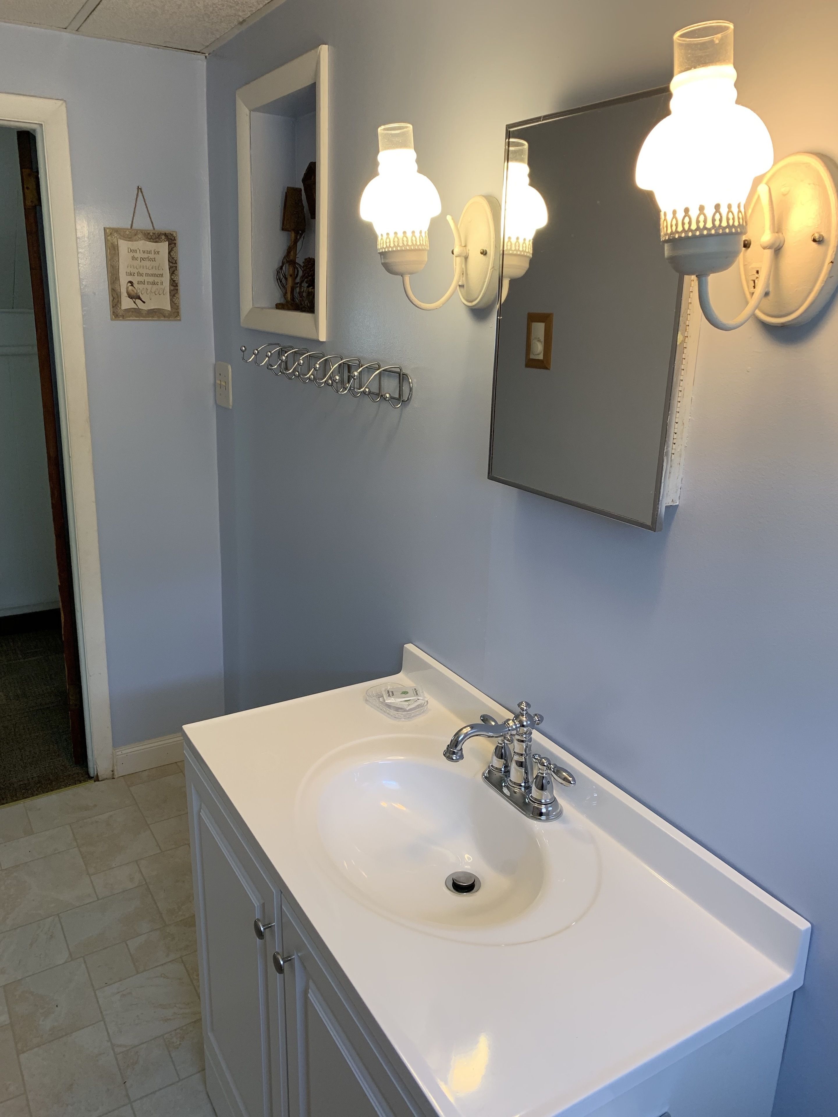 Une salle de bain avec un lavabo blanc, deux appliques murales, un miroir et un panneau décoratif.