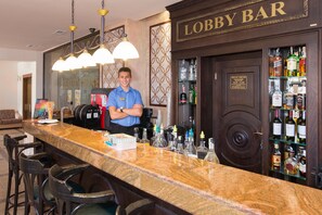 Um bar no hall com balcão de mármore, banquetas e diversos frascos de bebidas.