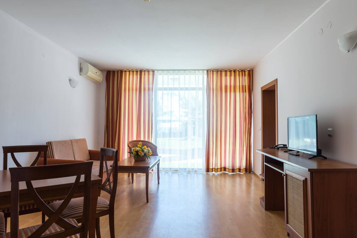 Una habitación con una mesa de comedor, sillas, un televisor y cortinas.