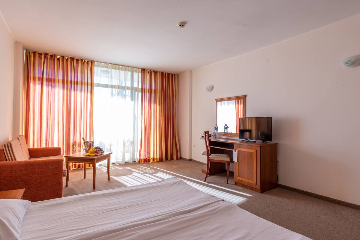 Habitación de hotel con cama, escritorio, silla, televisor y ventana con cortinas.