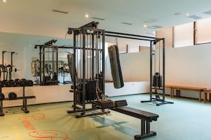 Academia com equipamentos de musculação, bancos e um saco de pancadas.