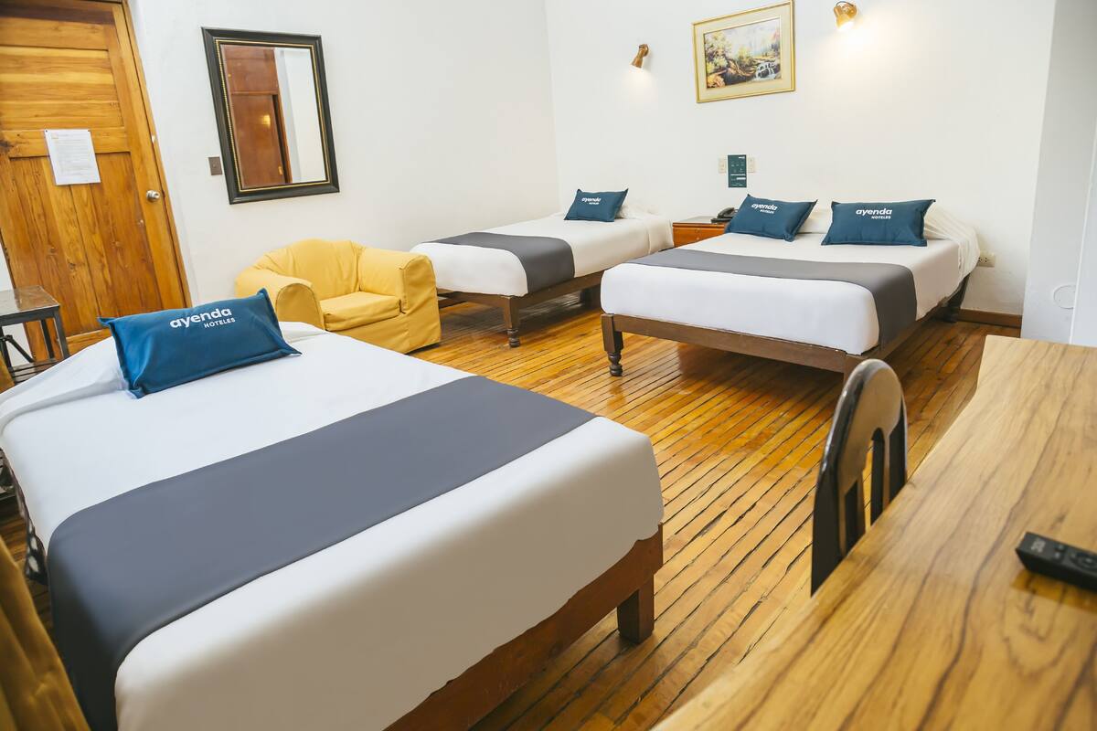 Habitación de hotel con dos camas individuales, suelo de madera, un sillón amarillo y un escritorio con silla.
