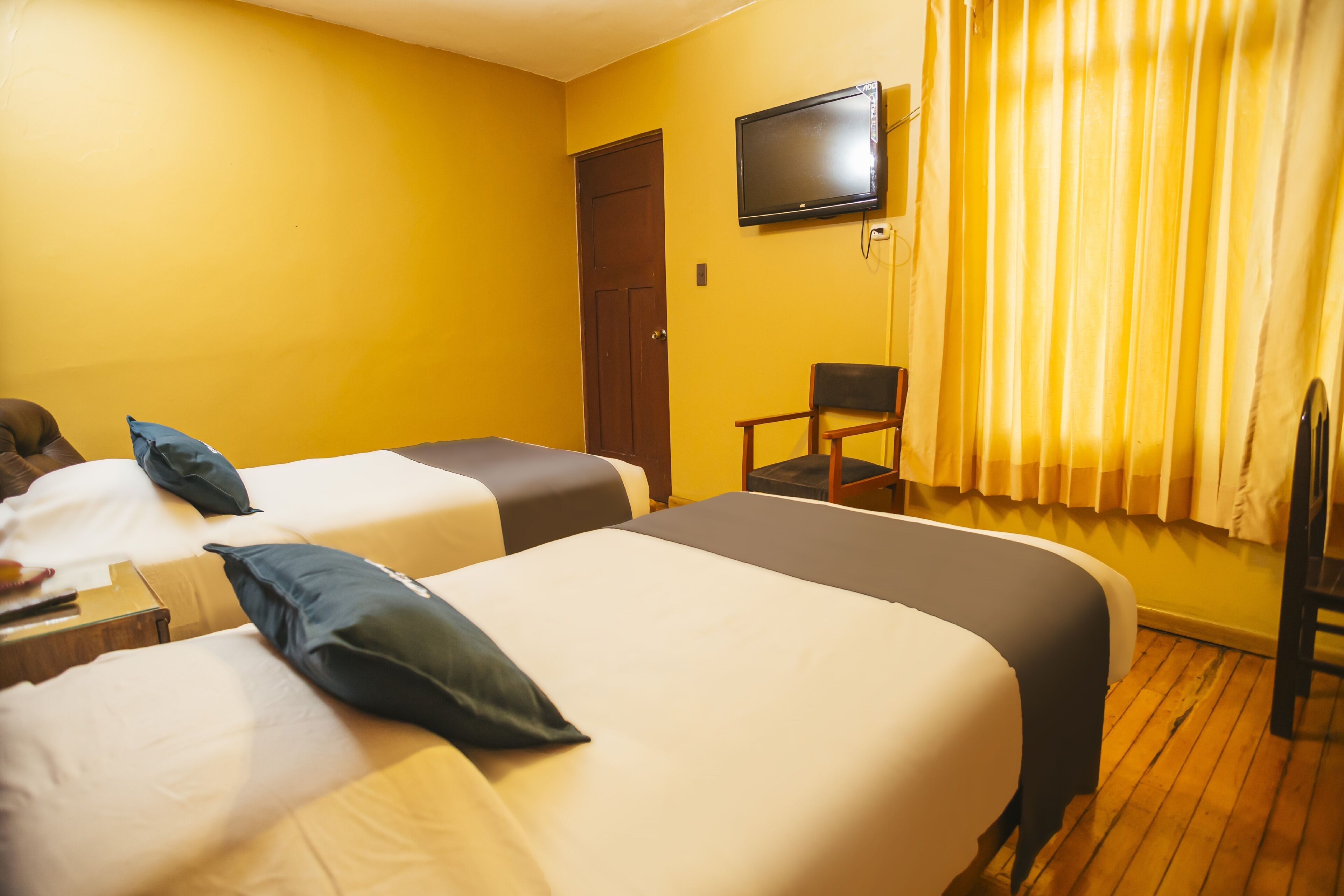 A hotel room with two beds, a TV, a chair, and a door.