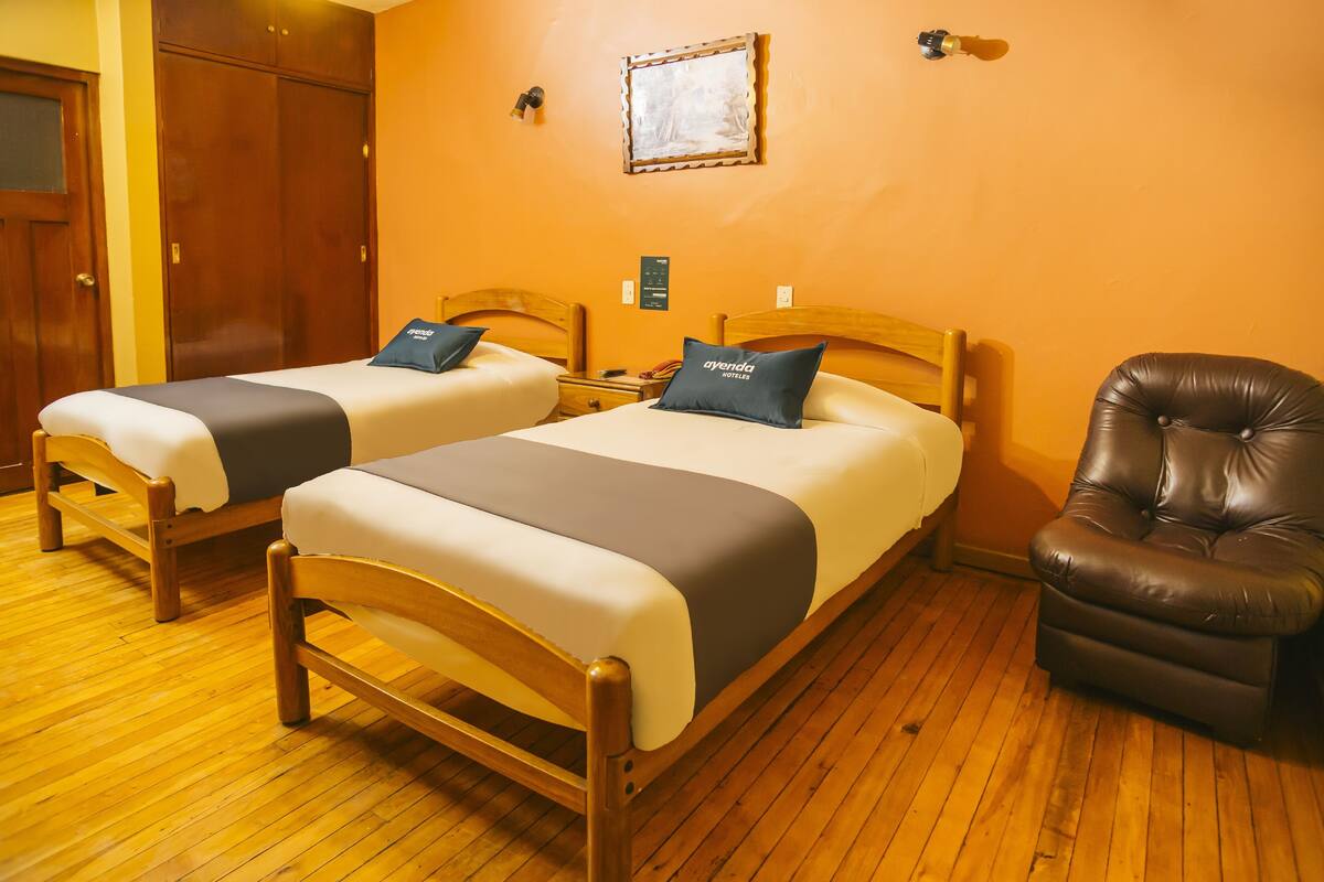 Una habitación de hotel con dos camas de madera, un sillón de cuero y suelo de madera.