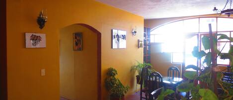 Una habitación con paredes amarillas, una zona de comedor con sillas y una mesa, y una escalera que lleva a otro nivel.
