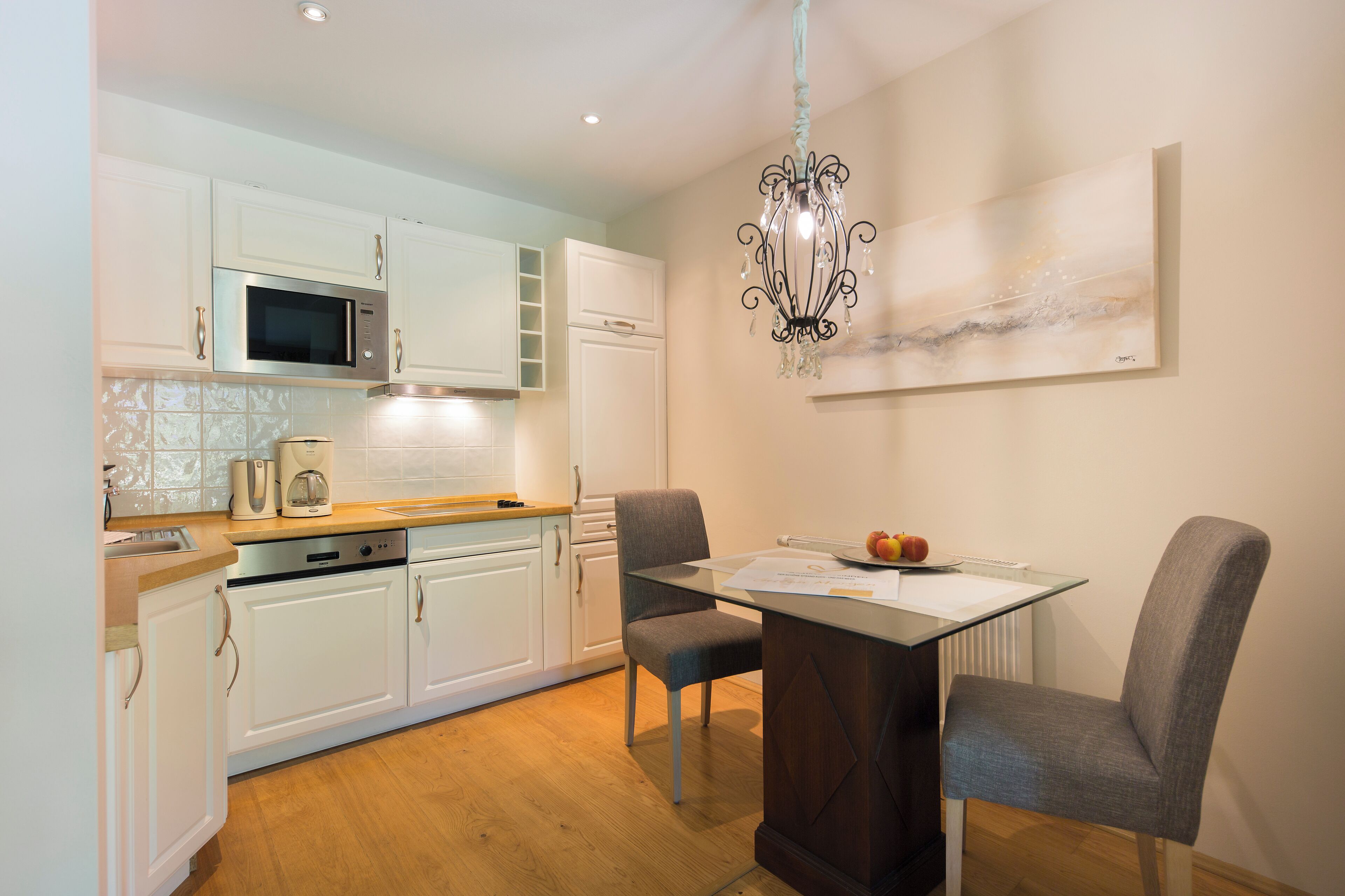 Een moderne keuken met witte kasten, een magnetron, een koffiezetapparaat en een eethoek met een tafel en twee stoelen.