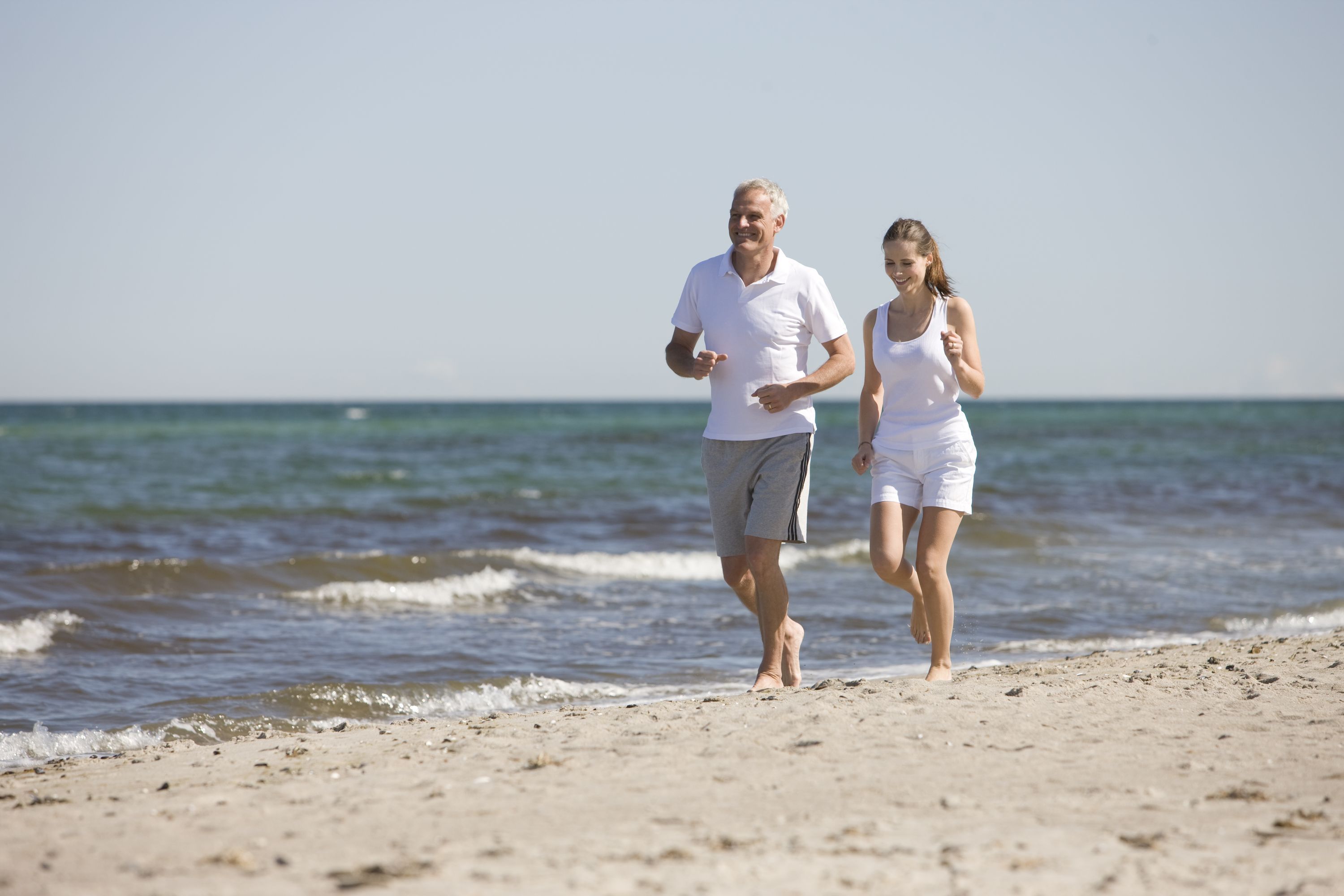 Zwei Personen gehen am sandigen Strand entlang, das Meer ist im Hintergrund zu sehen.