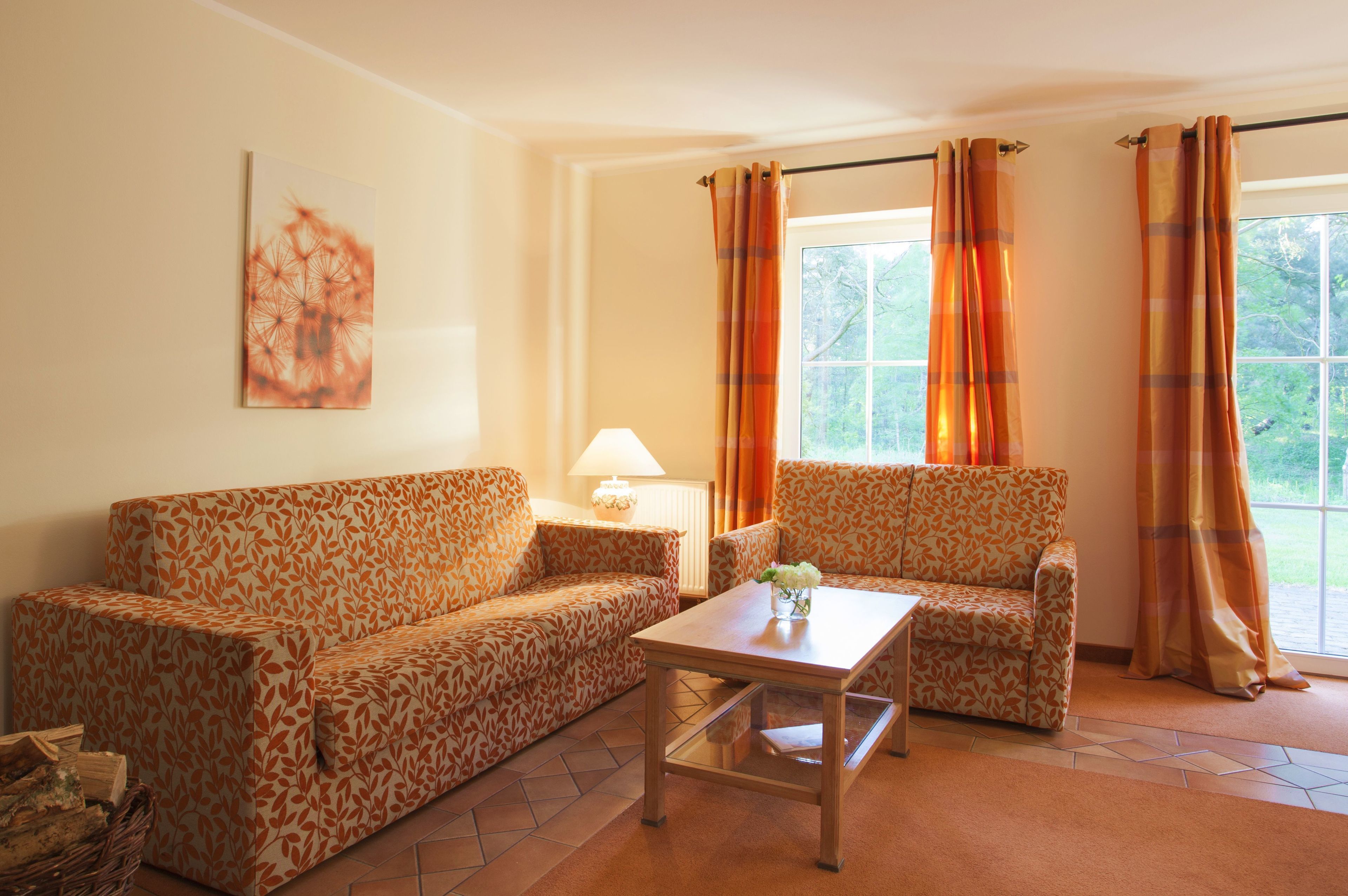 Un salon avec des canapés à motifs, une table basse, une lampe et une fenêtre avec des rideaux.
