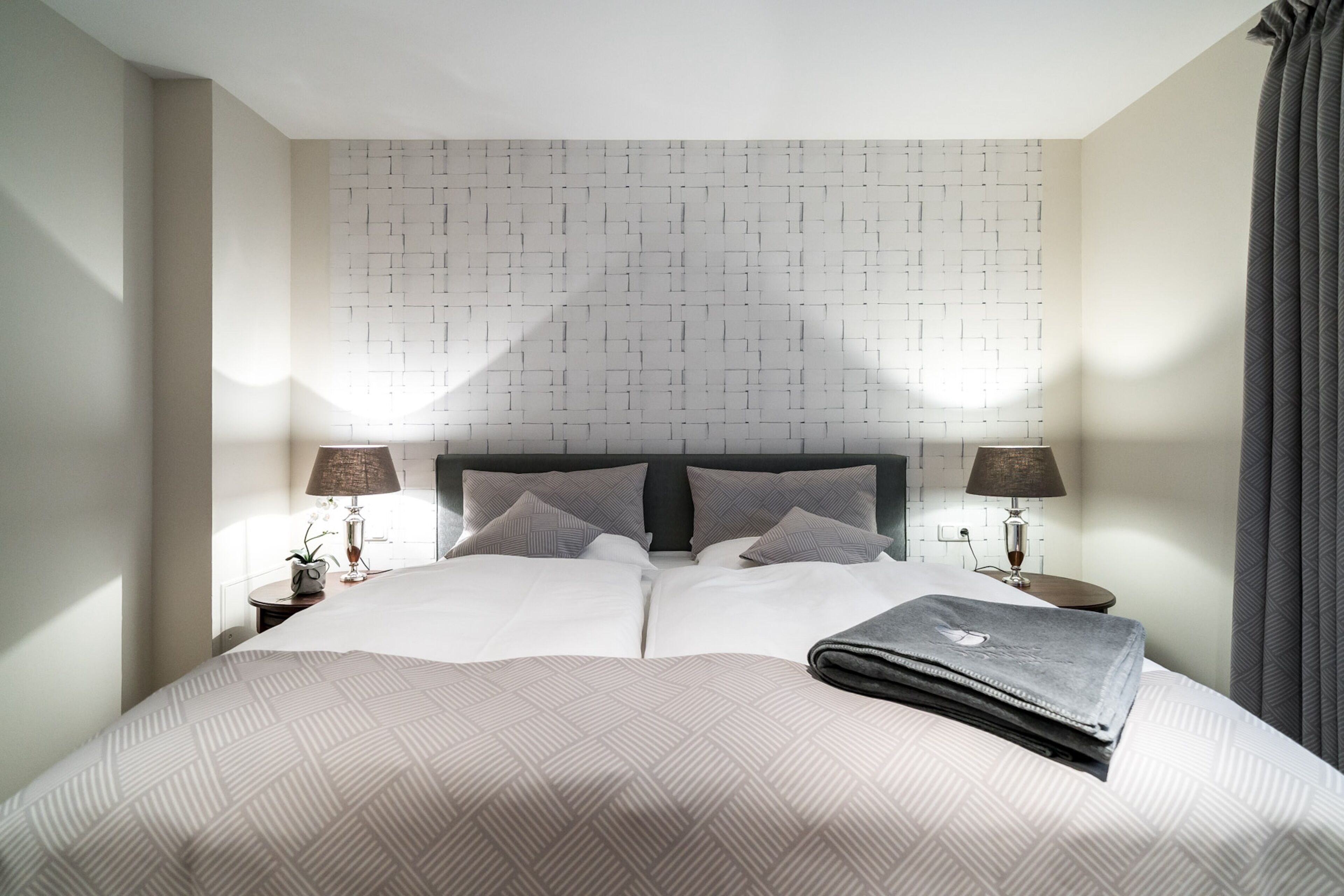 A neatly made bed with a patterned bedspread, two bedside lamps, and a headboard with a geometric pattern.
