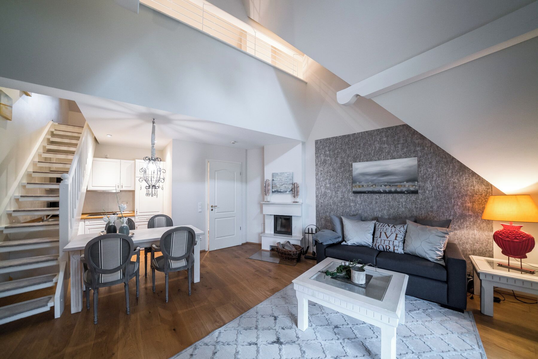 Un appartement moderne de style « loft » comprenant un coin repas, un salon avec un canapé et une cheminée, ainsi qu’un escalier menant à un niveau supérieur.
