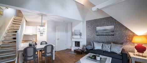Un appartement moderne de style « loft » comprenant un coin repas, un salon avec un canapé et une cheminée, ainsi qu’un escalier menant à un niveau supérieur.