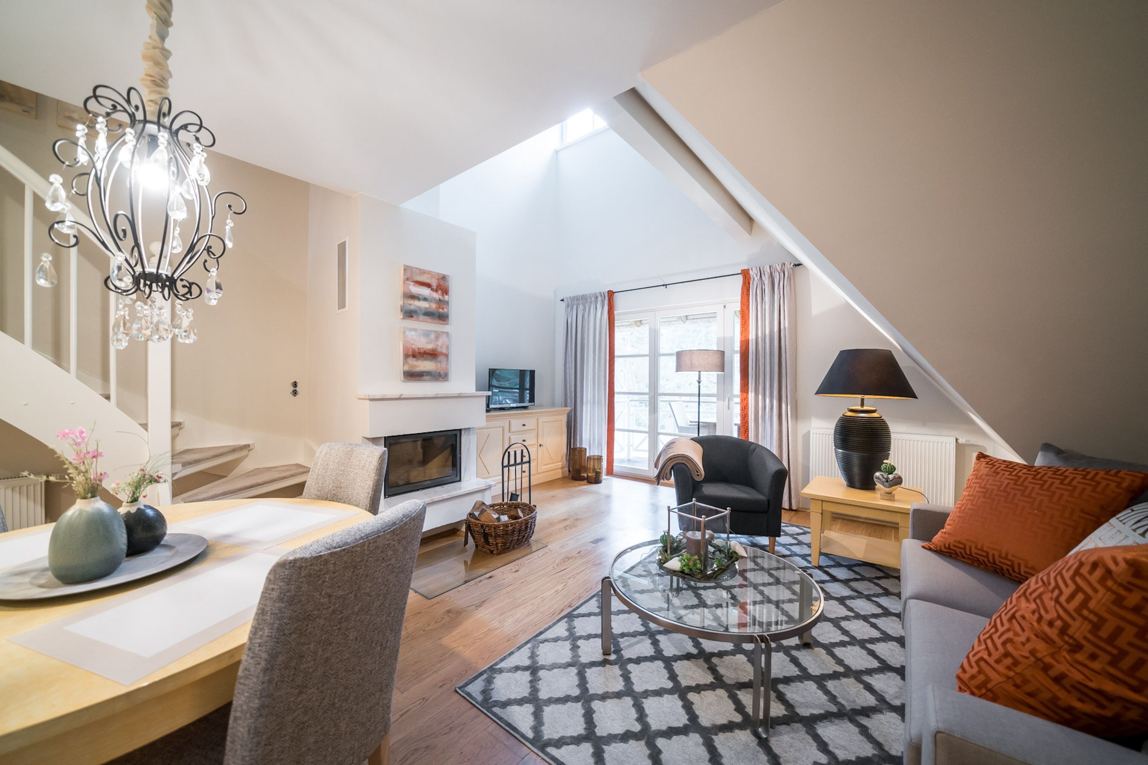 Una sala de estar moderna con chimenea, un candelabro y un comedor con mesa y sillas.