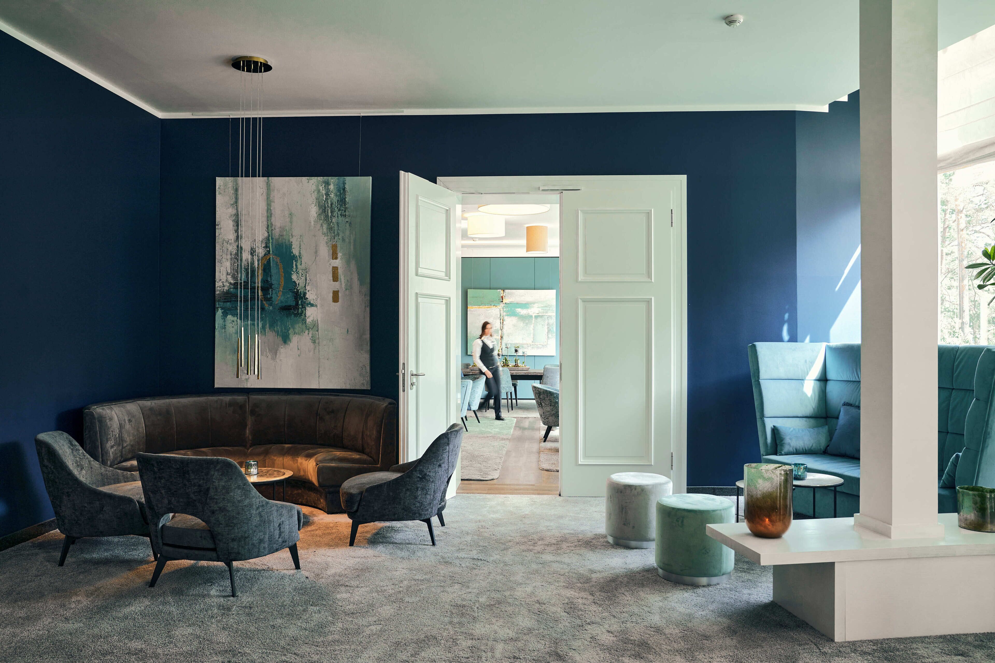 Un salón moderno con pared azul oscuro, un cuadro abstracto grande, un sofá de cuero oscuro y una mesita de centro redonda.